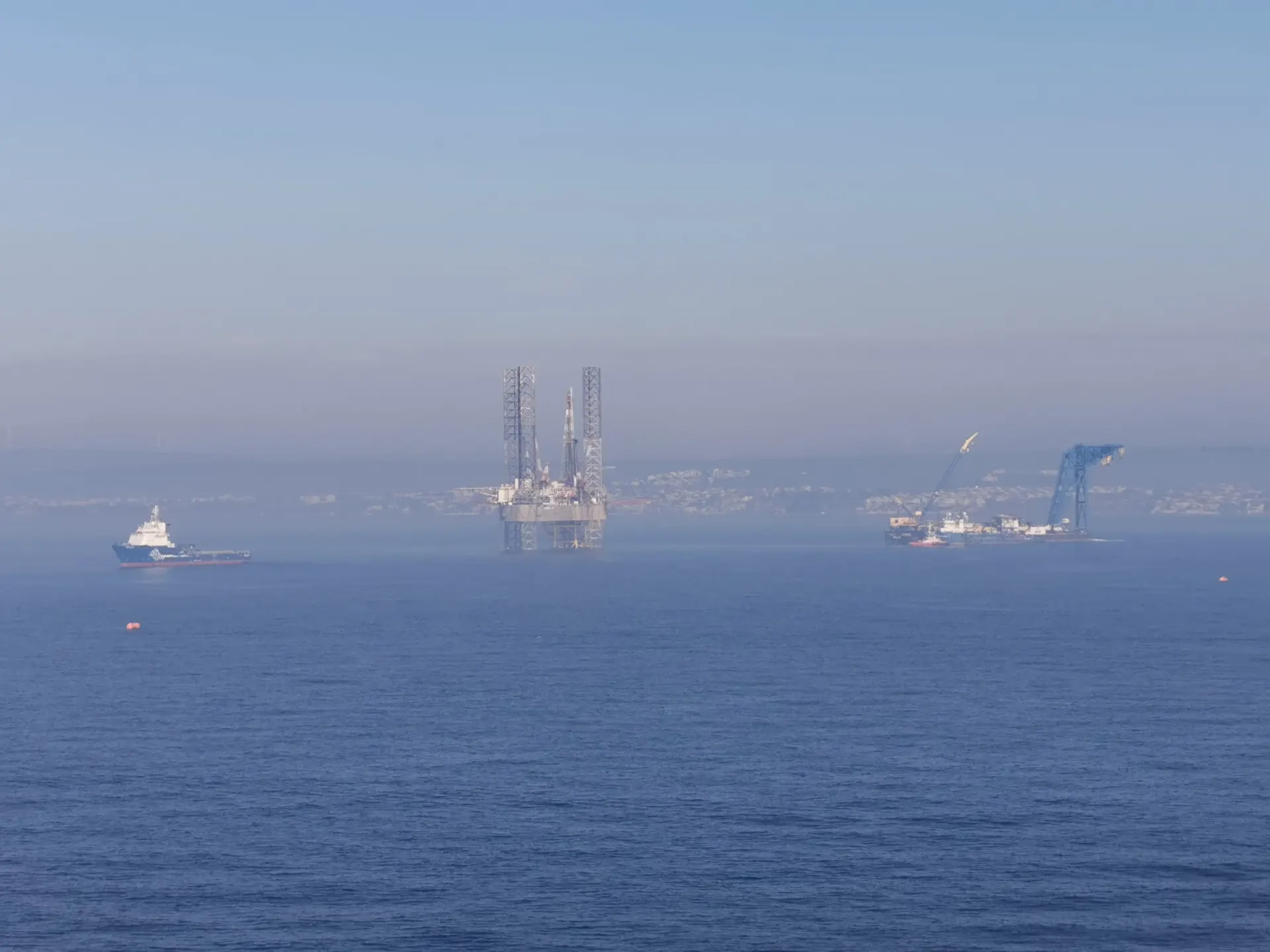Offshore jack-up rig with support boats in morning mist