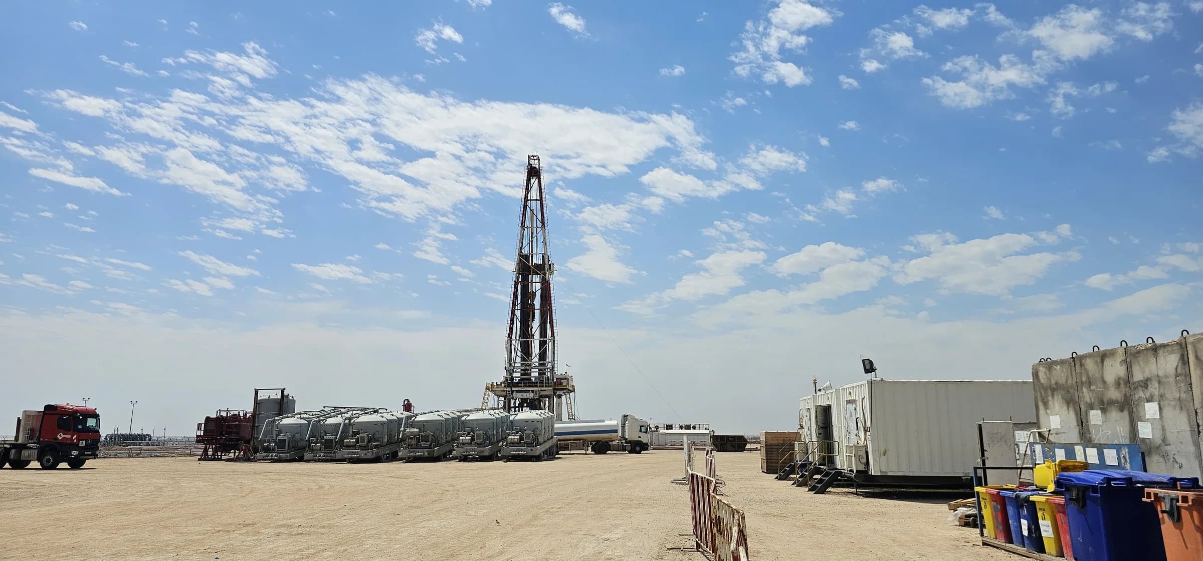 Rig site equipment yard with trucks and pump skids under open sky